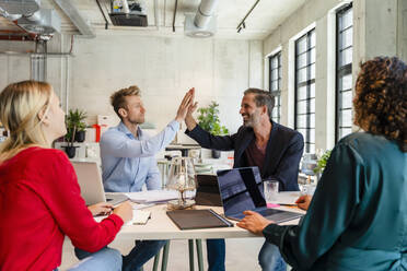 Businessmen giving high-five in meeting with colleagues at office - DIGF16660