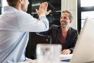 Glücklicher Geschäftsmann gibt einem Mitarbeiter in einer Besprechung ein High-Five - DIGF16661