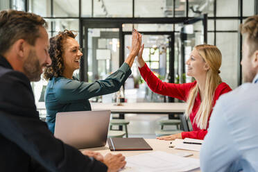 Businesswomen giving high-five in meeting with coworkers at office - DIGF16667