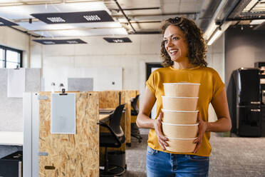 Smiling businesswoman holding lunch boxes at coworking office - DIGF16677