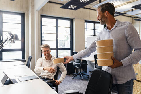 Geschäftsmann gibt Lunchpaket an Mitarbeiter im Büro - DIGF16683