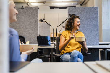 Smiling businesswoman having food with coworker in office - DIGF16699