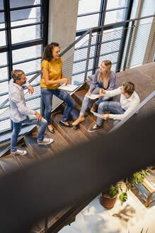 Businesswoman discussing with coworkers on steps in office - DIGF16737