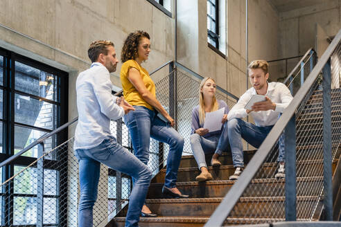 Young businessman showing tablet PC to coworkers on steps - DIGF16740