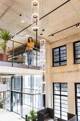 Businesswoman standing at railing in office - DIGF16752