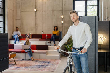 Junger Geschäftsmann mit Fahrrad im Coworking-Büro - DIGF16780