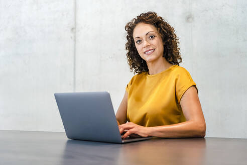 Lächelnde Geschäftsfrau mit Laptop am Schreibtisch - DIGF16797