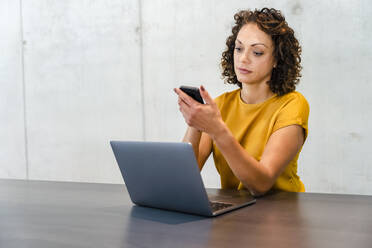 Female entrepreneur with laptop using mobile phone at desk - DIGF16800