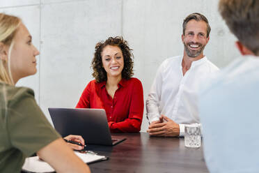 Smiling coworkers with laptop in business meeting - DIGF16803