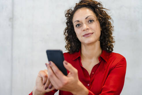 Unternehmerin hält Mobiltelefon vor einer Wand - DIGF16828