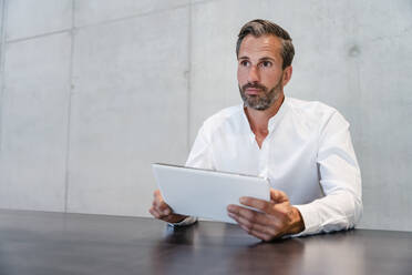 Nachdenklicher Geschäftsmann hält Tablet-PC am Schreibtisch - DIGF16840