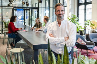 Lächelnder Geschäftsmann mit verschränkten Armen in einem Coworking-Büro - DIGF16855