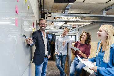 Smiling businessman pointing at whiteboard in meeting with colleagues at office - DIGF16883