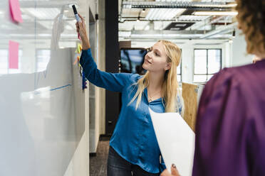 Junge Geschäftsfrau prüft Diagramm bei der Arbeit mit einem Kollegen im Büro - DIGF16892