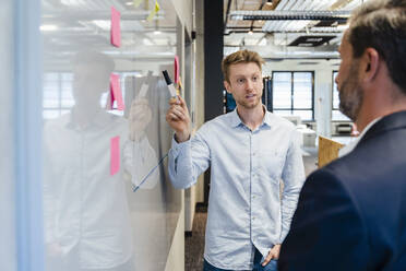 Young businessman with pen explaining colleague over graph at whiteboard - DIGF16895