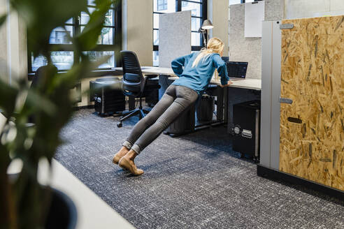 Junge Geschäftsfrau macht Liegestütze auf dem Schreibtisch im Büro - DIGF16905