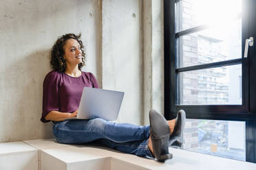 Smiling female entrepreneur with laptop at office - DIGF16911