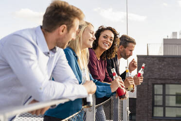 Kollegen trinken etwas, während sie sich auf das Geländer der Terrasse stützen - DIGF16934