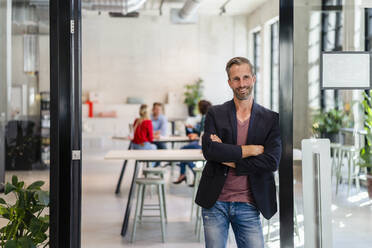 Smiling businessman with arms crossed at office entrance - DIGF16956