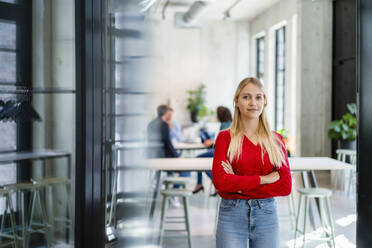 Blond businesswoman standing with arms crossed at office entrance - DIGF16958