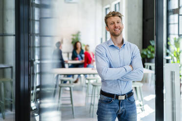 Smiling businessman with arms crossed in office - DIGF16966