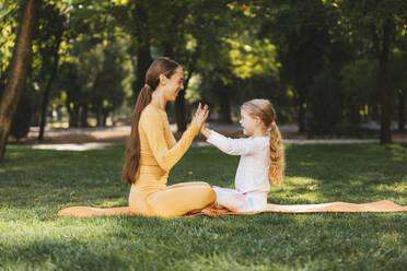 Smiling daughter touching mother's hands on exercise mat in park - OYF00622