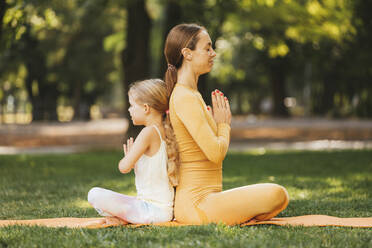 Mother and daughter with hands clasped meditating back to back in park - OYF00630