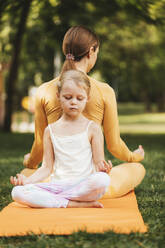 Girl with mother in lotus position on exercise mat at park - OYF00632