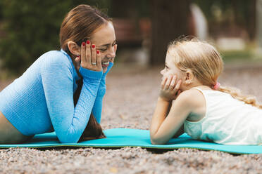 Smiling mother and daughter looking at each other while lying on exercise mat - OYF00638