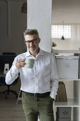Lächelnder Geschäftsmann mit Kaffeebecher im Büro - GIOF13940