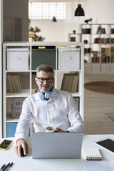 Smiling businessman in front of laptop at office - GIOF13946