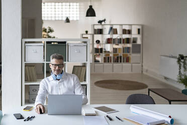 Lächelnder Geschäftsmann bei der Arbeit am Laptop im Büro - GIOF13947