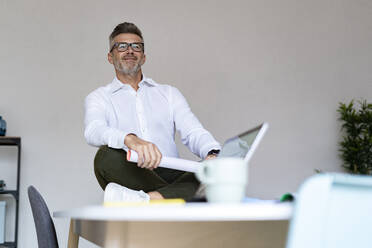 Smiling businessman with document on desk in office - GIOF13954