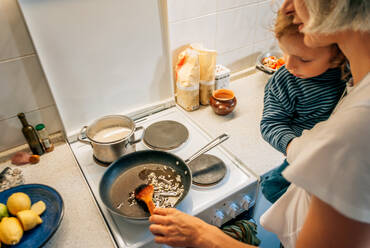Eine Frau kocht zu Hause ein Abendessen mit einem Kind im Arm - CAVF94932