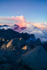 Nächtliche Landschaft mit einem ausbrechenden Vulkan im Hintergrund und einem Wolkenmeer, das die Berge in einer sternenklaren Nacht von einem bewachsenen und felsigen Berg aus bedeckt. Vulkanausbruch auf der Cumbre Vieja in La Palma, Kanarische Inseln, Spanien, 2021 - ADSF31276