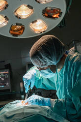 Tierarzt in sterilen Handschuhen mit chirurgischer Pinzette und Schere bei der Operation eines anonymen Tieres am Herzfrequenzmonitor im Krankenhaus - ADSF31292