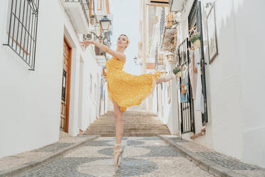 Full body of gorgeous female in pointe shoes performing graceful ballet movement with raised leg and arm - ADSF31294