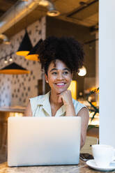 Positiv eingestellte Afroamerikanerin mit lockigem Haar, die auf einem Netbook tippt, während sie an einem Tisch arbeitet - ADSF31338