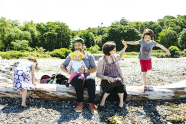 Wide view of a mother helping her daughter balance on driftwood - CAVF94938