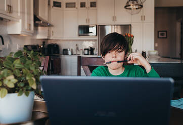 Young boy doing on school work online on computer at kitchen table. - CAVF94947