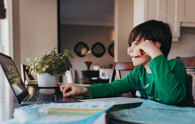 Young boy doing on school work online on computer at kitchen table. - CAVF94949