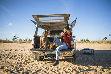 Young woman enjoying cup of coffee in the morning beach car camping - CAVF94964