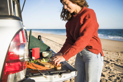 Junge Frau Tailgating Kochen während Strand Auto Camping allein - CAVF94966