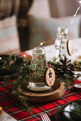 Weihnachtlich gedeckter Tisch mit Kranz und dekorativen Holzornamenten und rot karierter Tischdecke mit gelben Lichtern im Hintergrund - ADSF31379