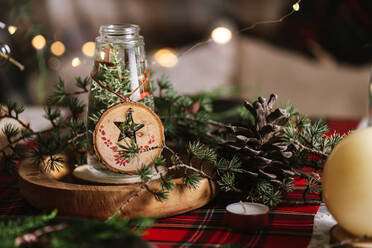 Weihnachtlich gedeckter Tisch mit Kranz und dekorativen Holzornamenten und rot karierter Tischdecke mit gelben Lichtern im Hintergrund - ADSF31381