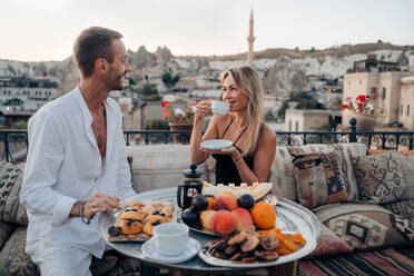 Content loving man and woman drinking tea and looking at each other while spending time together on terrace of cafe with pillows in Turkey Cappadocia - ADSF31388