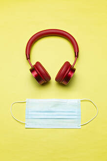 Studioaufnahme von roten drahtlosen Kopfhörern und einer Gesichtsschutzmaske vor gelbem Hintergrund - VGF00416