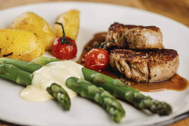 Steaks with sauce, potatoes, cooked cherry tomatoes and asparagus stalks - DAWF02073
