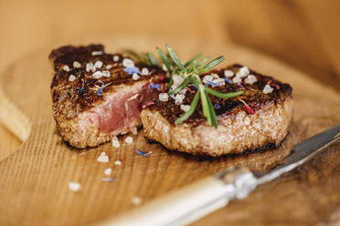 Close-up of ready-to-eat halved steak lying on wooden surface - DAWF02074