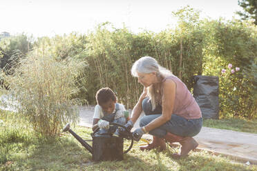 Boy and grandmother crouching with watering can at farm - MASF26423